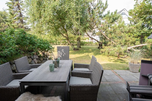 An outdoor patio with wicker furniture, a table, and a vase with dried plants.