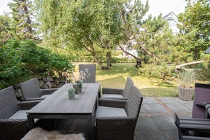 Eine Terrassengruppe im Freien mit Korbmöbeln, einem Tisch und einer Vase mit Trockenblumen.