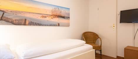 Een slaapkamer met een bed, een stoel, een televisie en een schilderij van een strand.