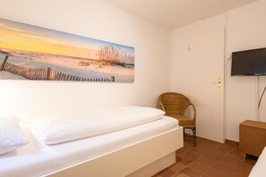 Un dormitorio con una cama, una silla, un televisor y un cuadro de una playa.