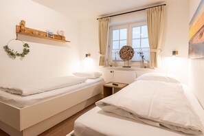 Ein Hotelzimmer mit zwei Einzelbetten, einem Holzboden mit Dekoration, einem Fenster mit Vorhängen und einer Wandleuchte.