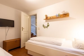 Ein Schlafzimmer mit einem Bett, einer Holzkommode, einem an der Wand befestigten Fernseher und einem Regal mit Büchern und Dekoration.