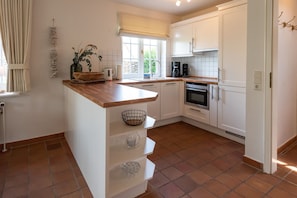 A compact kitchen with white cabinets, a wooden countertop, and a window with a view of greenery.