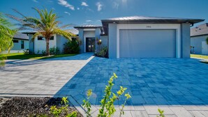 Una moderna casa a due piani con garage numero 1416, vialetto lastricato e una palma.