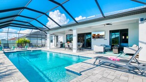 Una piscina con una veranda coperta, area salotto esterna e vista sullo skyline cittadino.