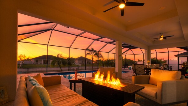 Zona relax esterna moderna con camino, posti a sedere e vista su piscina e tramonto.