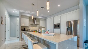 Una cucina moderna con isola centrale, sgabelli da bar, elettrodomestici in acciaio inossidabile e illuminazione a sospensione.