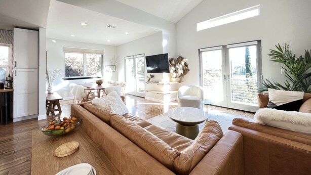 Amplia sala de estar con un sofá grande de cuero marrón, un comedor con mesa de madera y una cocina con refrigerador y televisor.