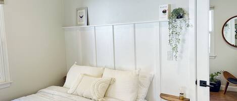 A bedroom with a bed, a bedside table, a hanging plant, and a mirror on the wall.