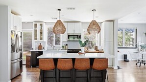 Una cocina moderna con una isla central, taburetes de bar, iluminación colgante y vistas al exterior.