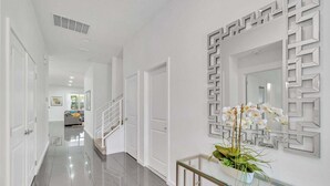A hallway with a glass console table, white doors, and a geometric wall decoration. - Vacation Paradise Home, Private Pool, Game Room (Kissimmee)