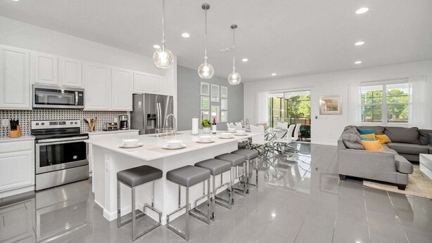 A modern kitchen with white cabinets, stainless steel appliances, a central island with bar stools, and pendant lighting. - Vacation Paradise Home, Private Pool, Game Room (Kissimmee)