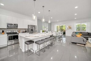 A modern kitchen with white cabinets, stainless steel appliances, a central island with bar stools, and pendant lighting. - Vacation Paradise Home, Private Pool, Game Room (Kissimmee)