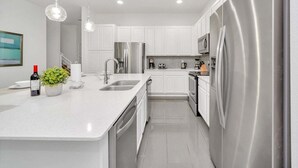 A modern kitchen with white cabinetry, stainless steel appliances, and a central island with a sink and a potted plant. - Vacation Paradise Home, Private Pool, Game Room (Kissimmee)