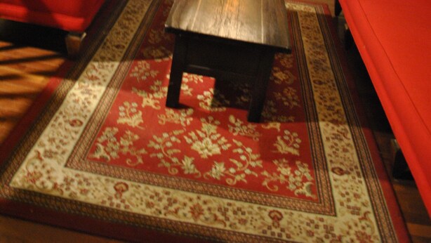 A room with a red sofa, a wooden coffee table, and a patterned rug. There are two mirrors on the walls, one above the coffee table and one above the sofa. - Newark Hansbury Multi Level House (Newark)