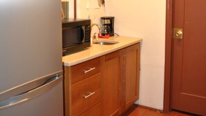 A compact kitchen with a refrigerator, microwave, coffee maker, and wooden cabinets. - Newark Hansbury Multi Level House (Newark)