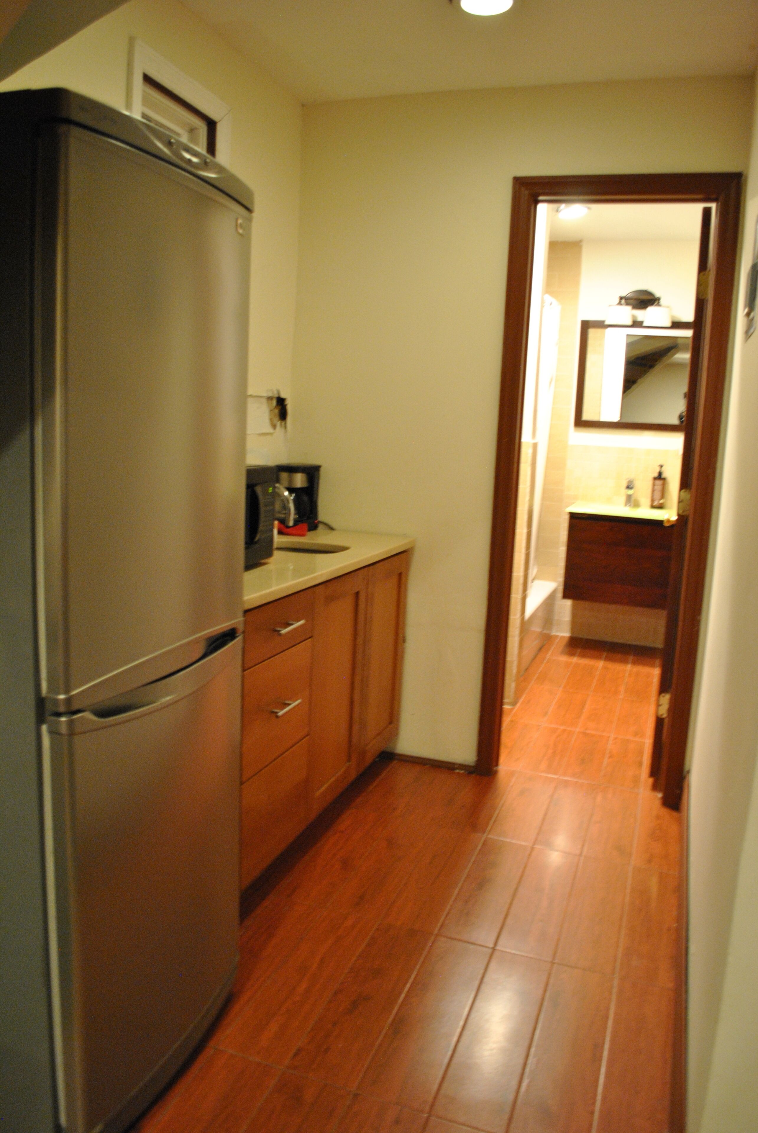 Una cocina estrecha con refrigerador, armarios de madera y piso de baldosas.