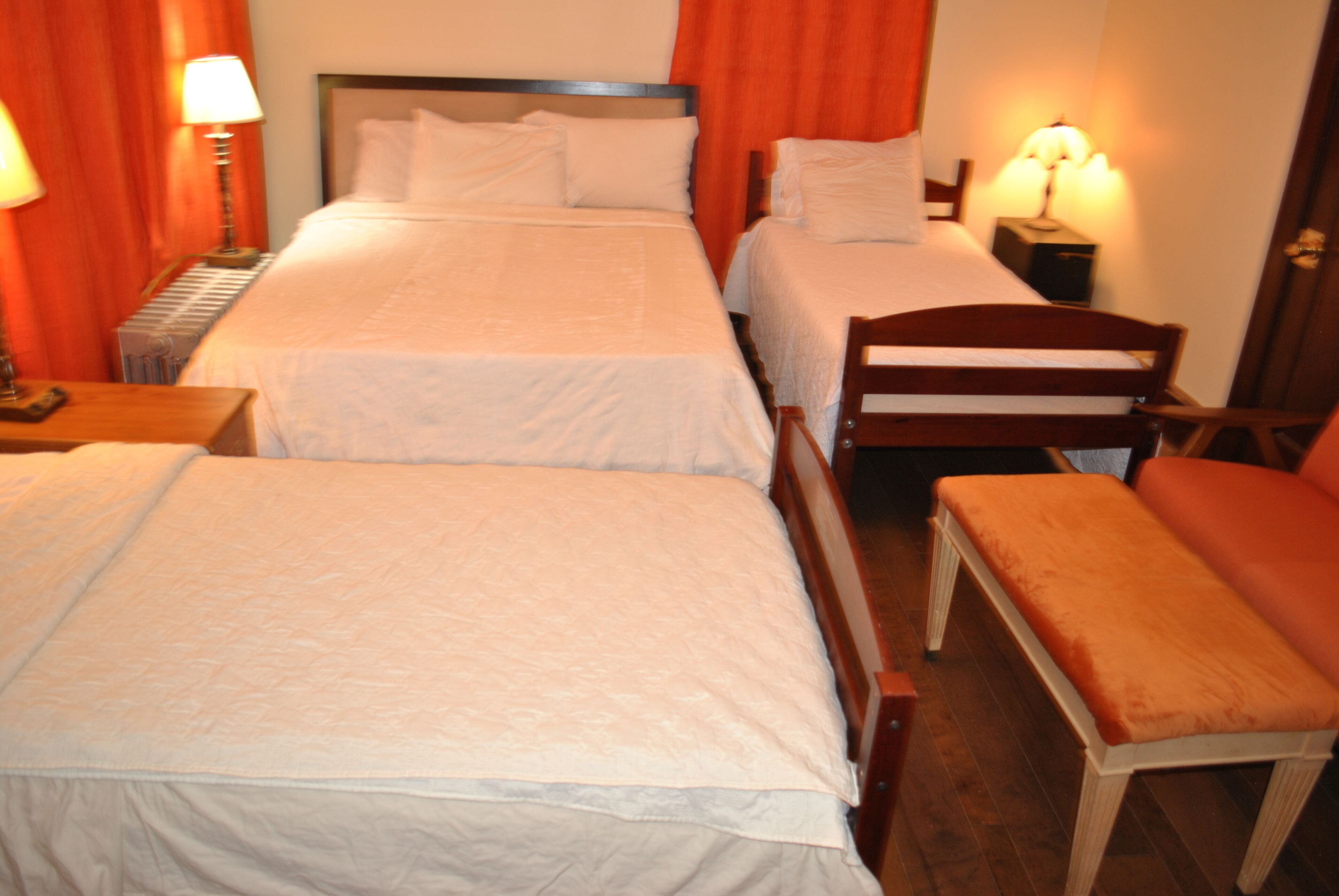 Een hotelkamer met twee enkele bedden, een houten bankje en een nachtkastje met een lamp.