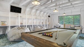 Een pooltafel met biljartballen, een zak stoel en een hangstoel in een kamer met witte muren en een hoge plafond.