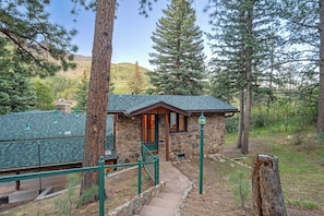 A stone cabin with a green roof, surrounded by trees and a mountain in the background.