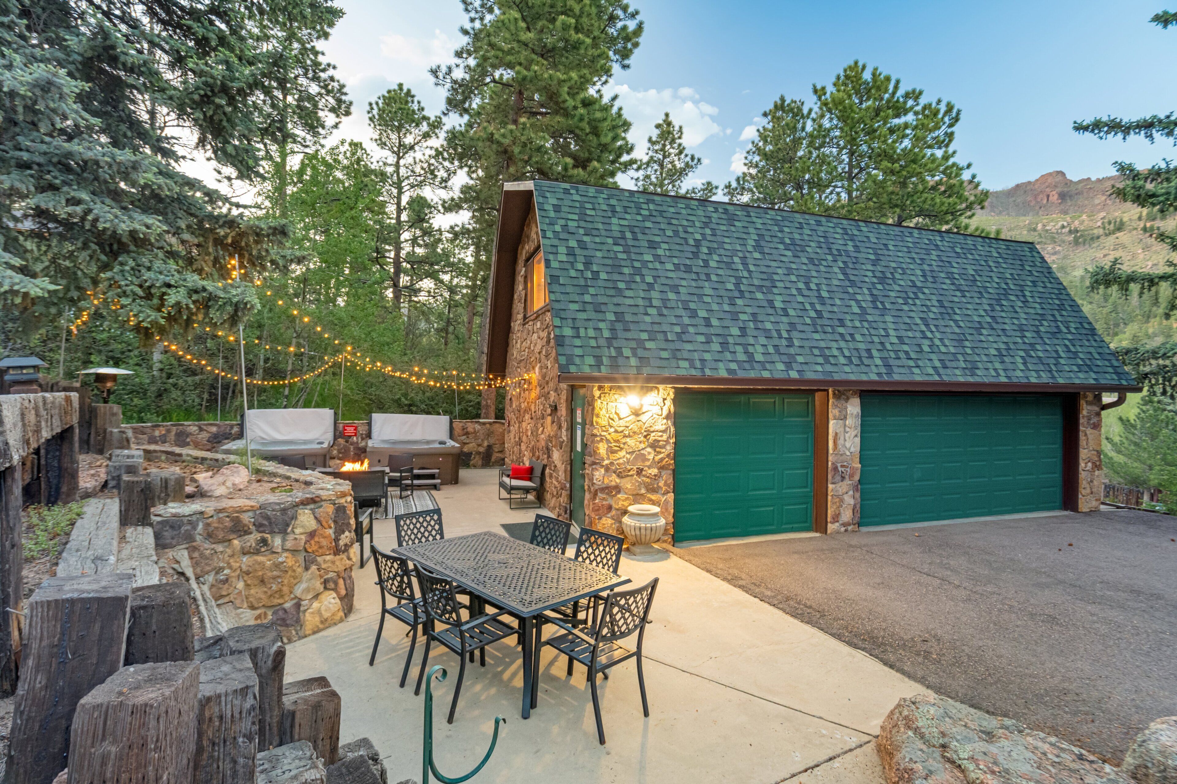 A cabin with a stone exterior, a green garage door, outdoor seating, and a fire pit.