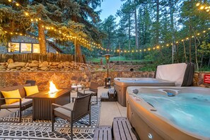 En udendørs terrasse med stenvæg, siddepladser, bålsted og hottubs.