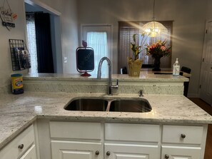 A kitchen with a granite countertop, stainless steel sink, white cabinets, a welcome sign, a potted plant, and a hanging light fixture. - Atl. Motor Speedway- Tucked Away In Comfort 4 Bedrooms totaling, 7 Beds (Fayetteville)