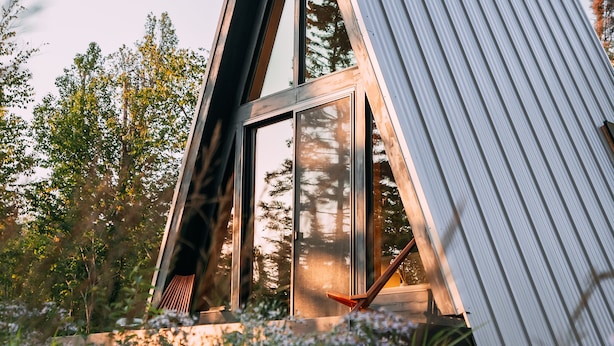 Un bâtiment moderne de forme triangulaire, doté de grandes fenêtres et d’une façade métallique, entouré d’une végétation luxuriante.