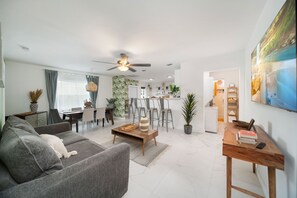 A modern living room with a grey sofa, wooden coffee table, and a dining area with chairs and a table.