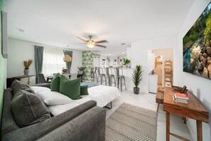 A modern living room with a sofa, a dining area, and a kitchen in the background. - Tropical Marlins House (Miami)