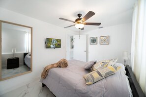 A bedroom with a bed, a ceiling fan, a large mirror, and artwork on the walls.