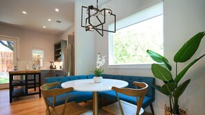 Eine moderne Küche mit Backofen, ein Essbereich mit rundem Tisch und blauen Sitzmöglichkeiten sowie ein großes Fenster mit Blick auf Grünflächen.