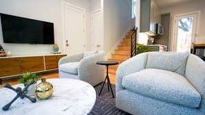 Ein modernes Wohnzimmer mit einem Marmortisch, zwei grauen Sofas mit Struktur und einem kleinen runden Tisch. Eine Treppe führt auf eine obere Ebene.