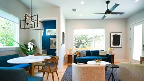 Ein modernes Wohnzimmer mit einem blauen Sofa, einem runden Esstisch und einem Deckenventilator.