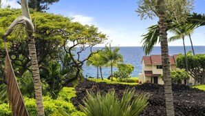 A tropical garden with a view of the ocean and a building with a red roof.
