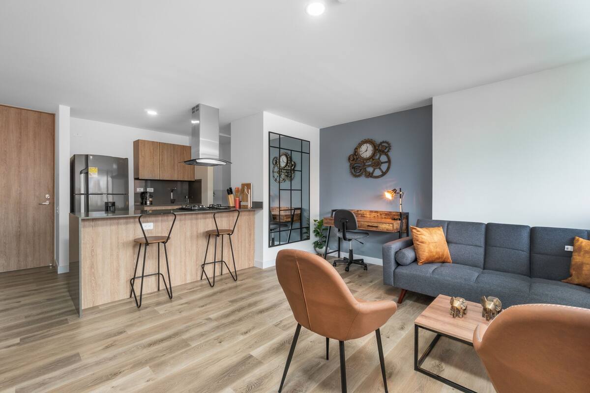 Una cocina moderna con una isla central, armarios de madera y un comedor con sofá y mesa de centro.