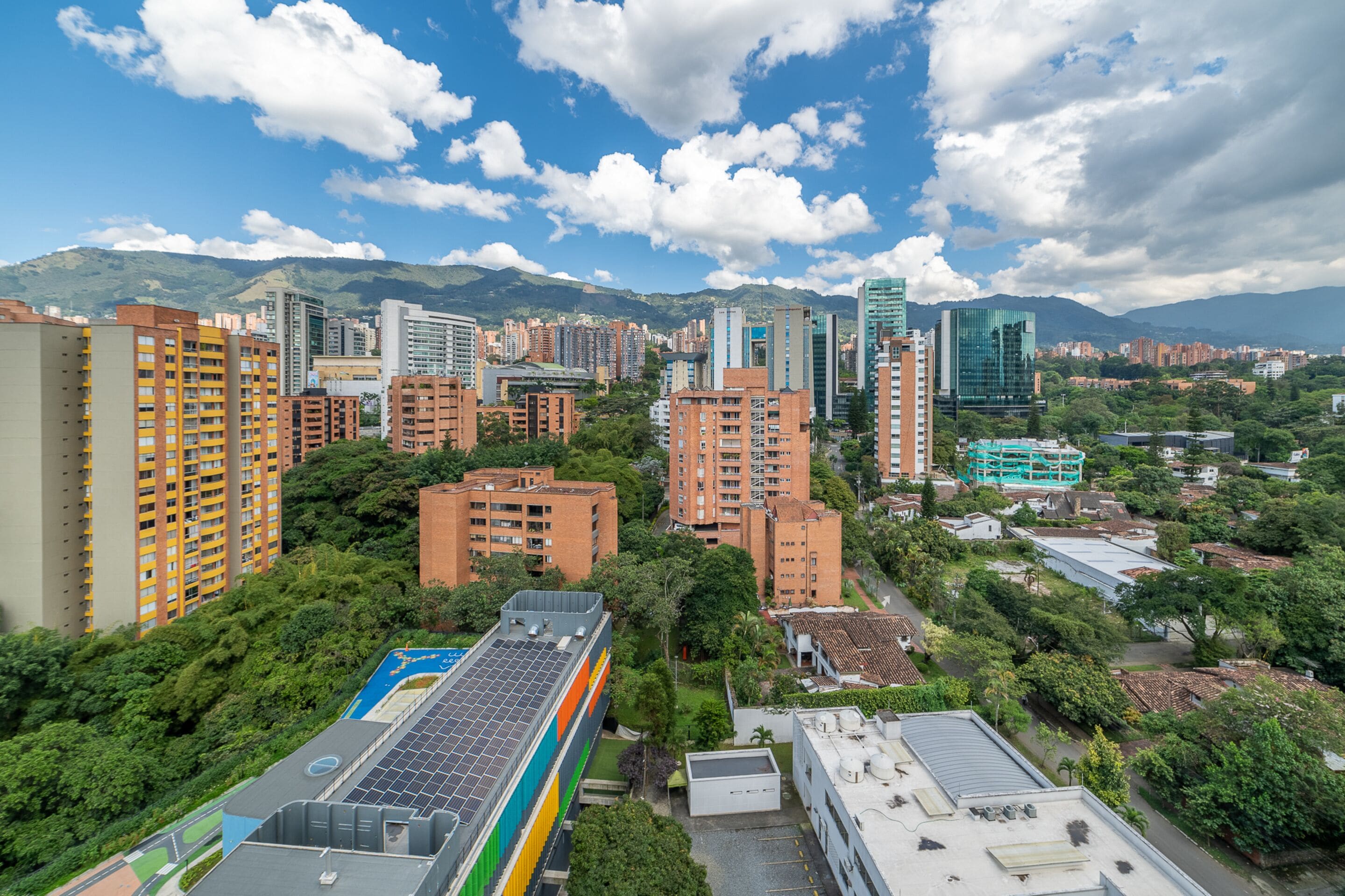 A cityscape with high-rise buildings, a mix of residential and commercial structures, and a mountainous backdrop.