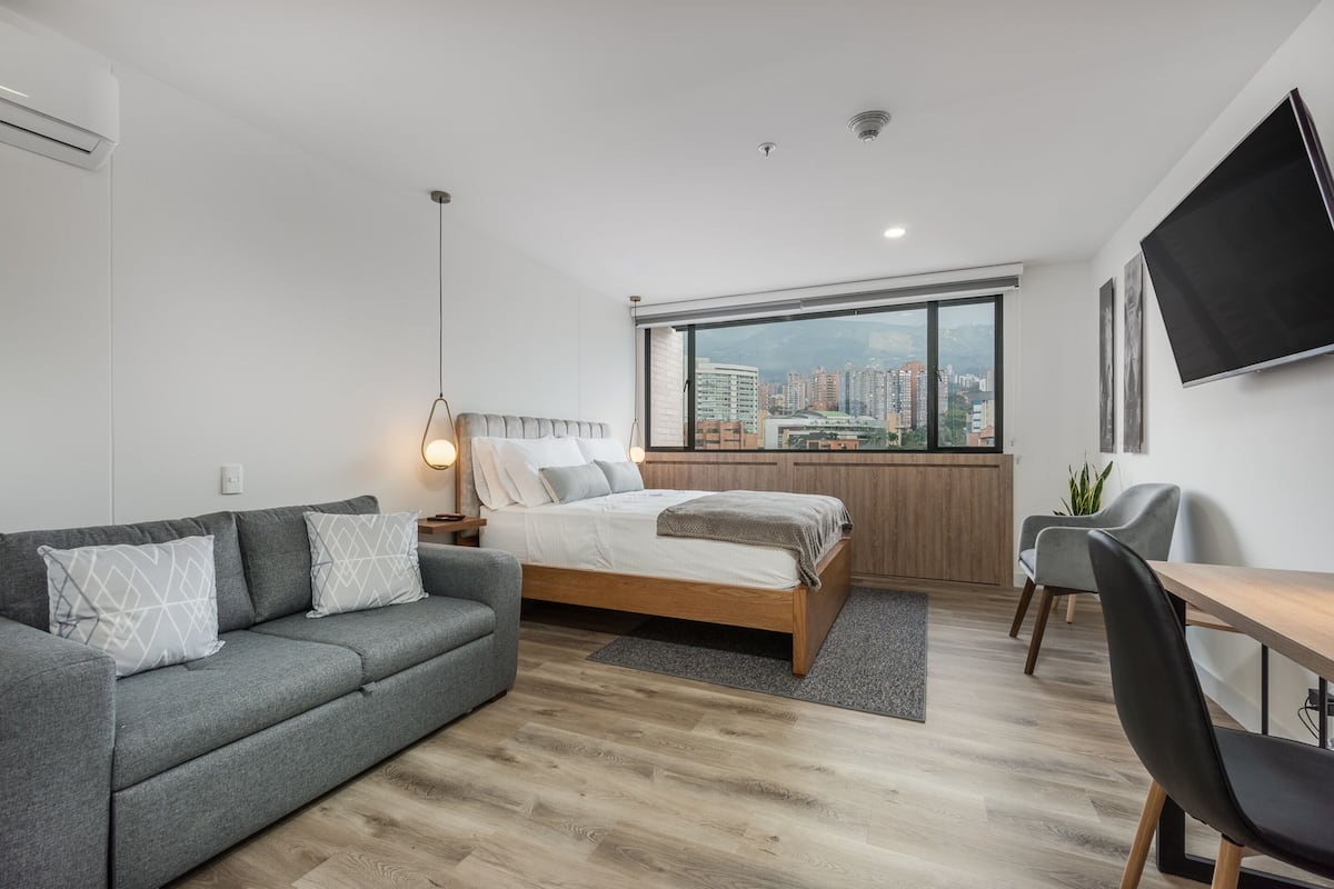 Un dormitorio moderno con cama, sofá gris y escritorio.