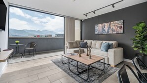 Un salon moderne avec une grande fenêtre, un canapé, une table basse et une vue sur les montagnes.