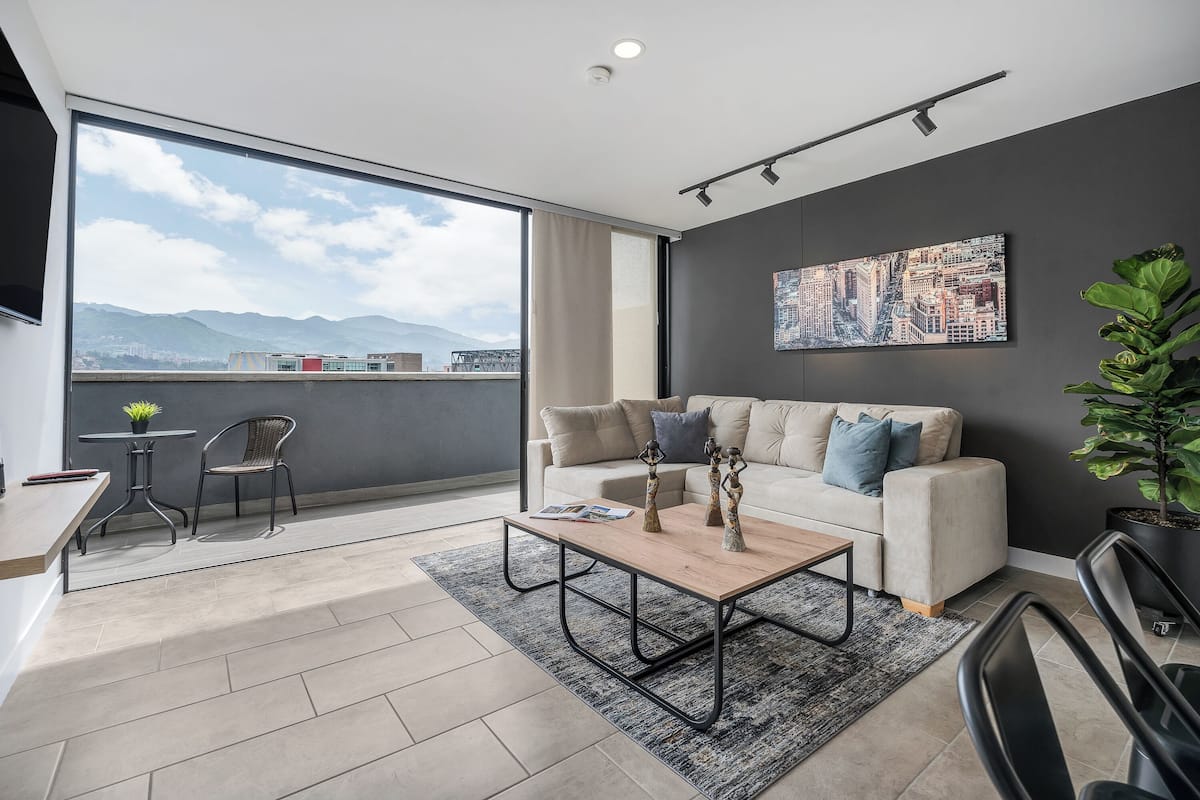 Una sala de estar moderna con un ventanal grande, un sofá, una mesa de centro y vistas a montañas.