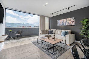 Una sala de estar moderna con un ventanal grande, un sofá, una mesa de centro y vistas a montañas.