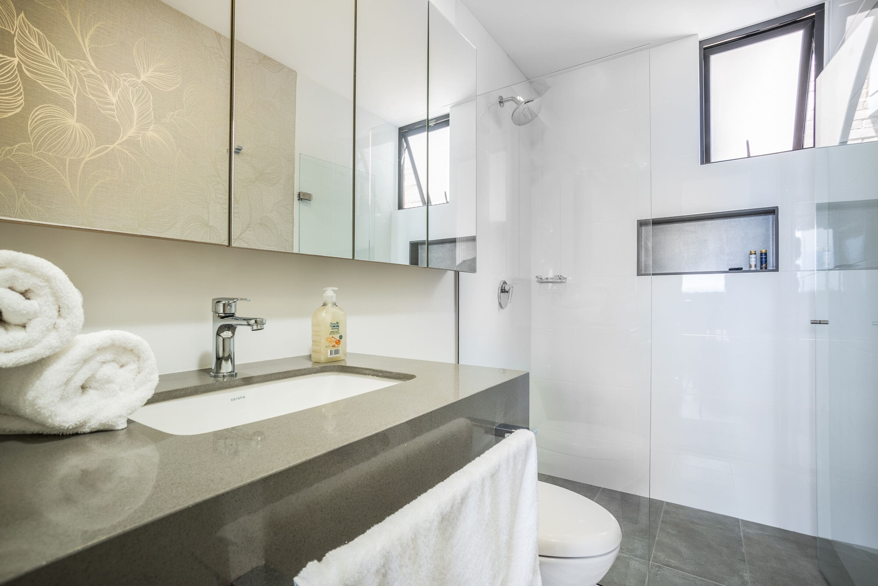 A modern bathroom with a large mirror, a sink, a toilet, and a shower.
