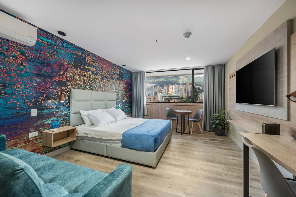 Habitación de hotel moderna con una cama grande, un escritorio, una silla y vistas a la ciudad a través de la ventana.
