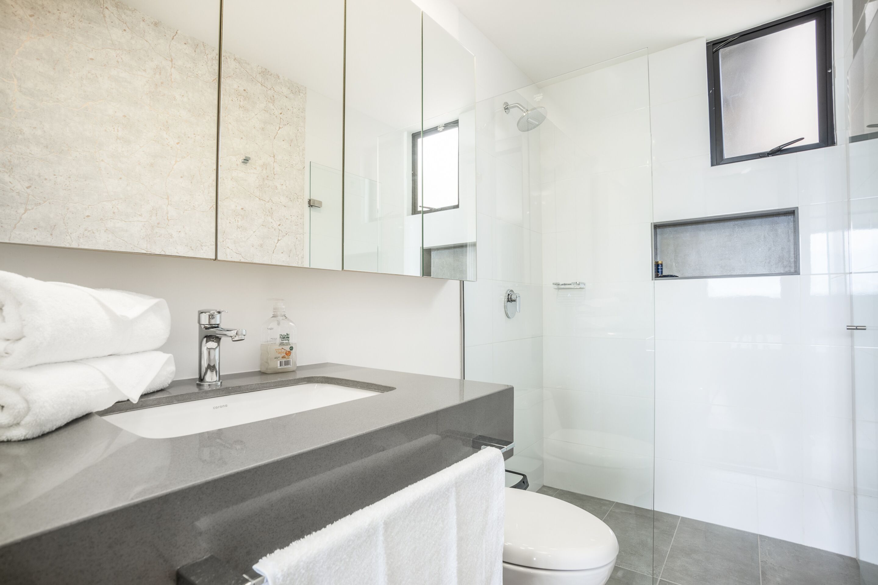 A modern bathroom with a large mirror, a sink, and a toilet.
