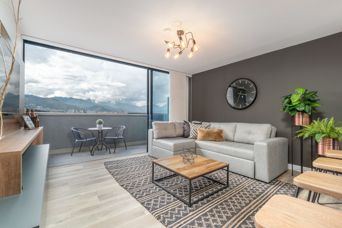 Una sala de estar moderna con un sofá gris, una mesa de centro y vistas a montañas a través de amplios ventanales.