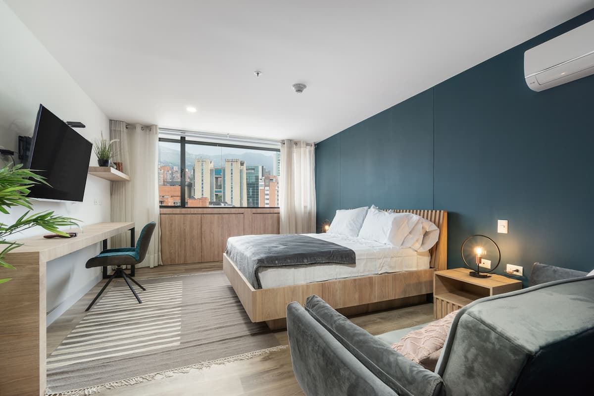 Habitación de hotel moderna con una cama grande, un escritorio con silla, televisor y vistas a la ciudad.
