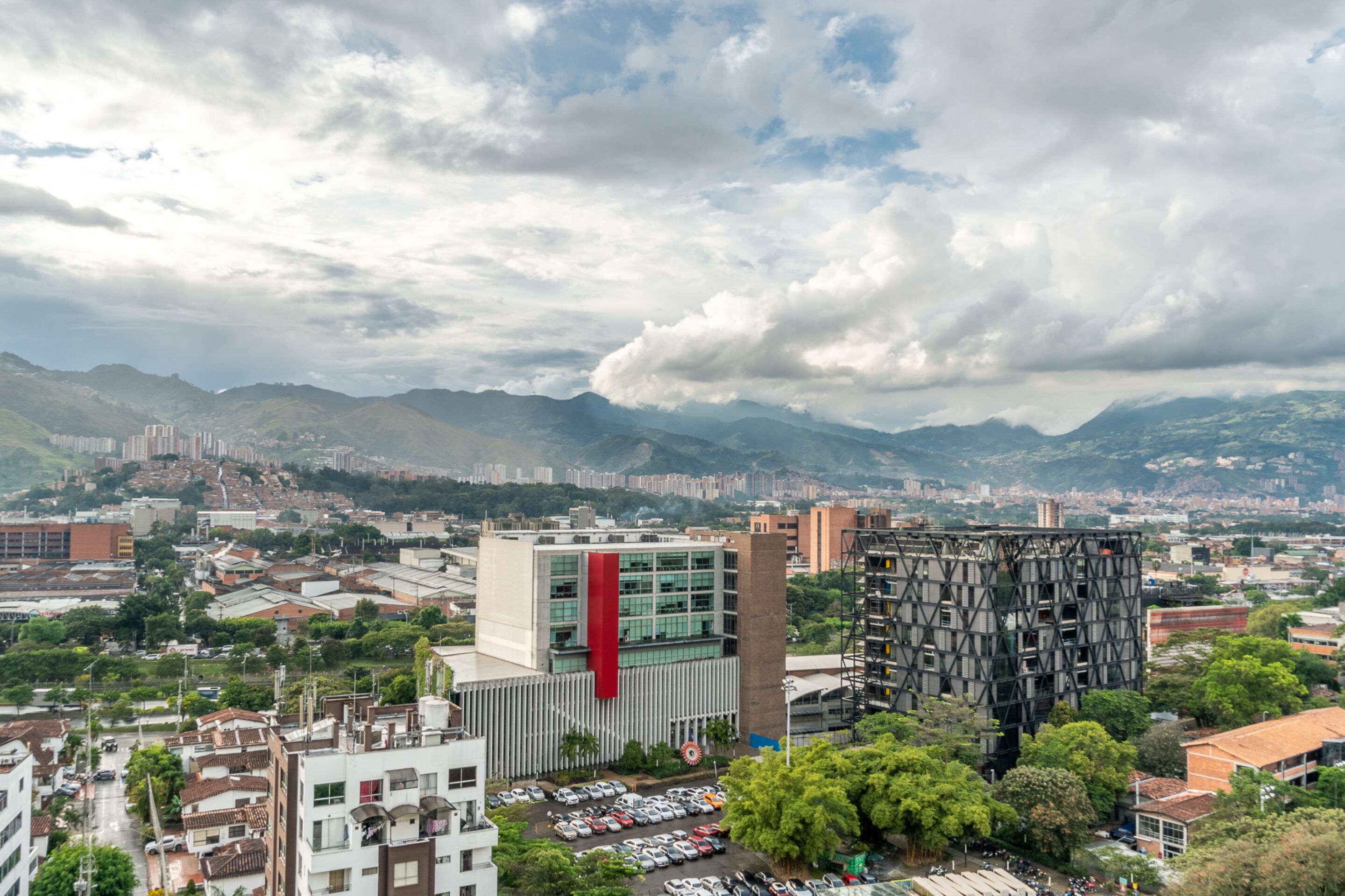 A cityscape with modern buildings, a prominent red structure, and surrounding greenery.