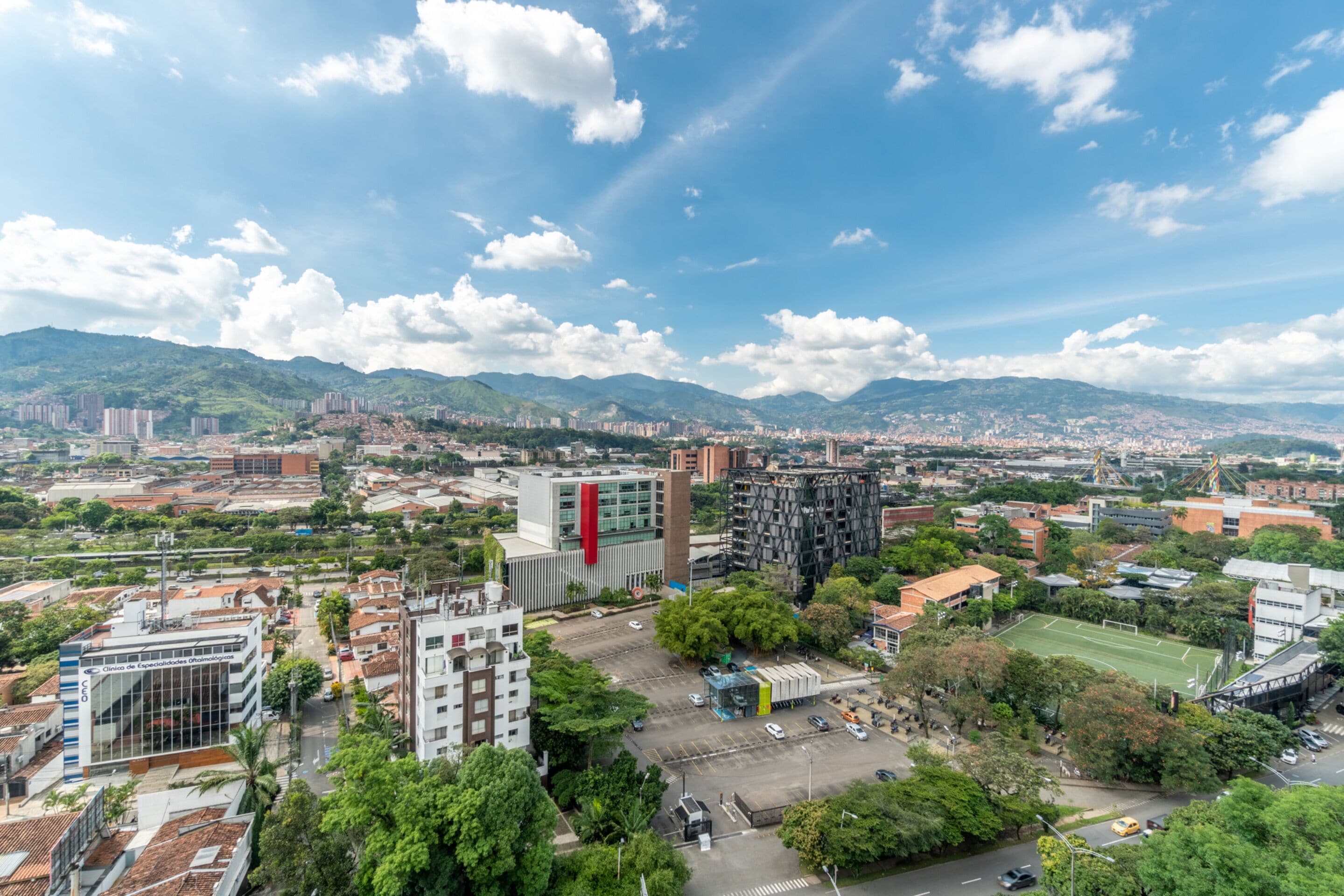 Paesaggio urbano con edifici moderni, un campo sportivo e aree verdi circostanti.