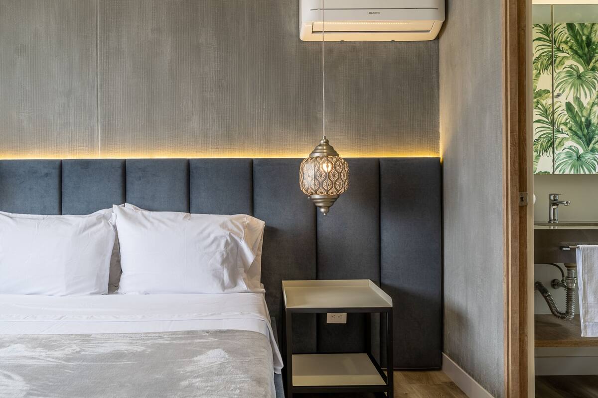 Un dormitorio moderno con cama, mesita de noche y aire acondicionado de pared.