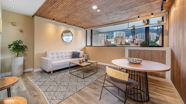 A modern living room with a white sofa, round coffee table, and a dining area with a wooden table and chairs.